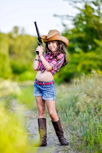 Niña con una pistola de juguete en la mano de pie en un campo — Foto de Stock