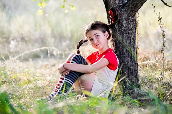 Trauriges Mädchen mit Zöpfen unter dem Baum — Stockfoto