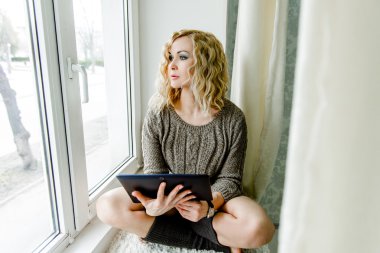 tablet ile pencerenin önünde oturan kız