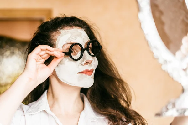 Frau trägt Maske aus Ton auf Gesicht auf und schaut in Spiegel. — Stockfoto