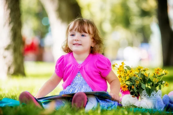 Niña sentada en el parque leyendo un libro — Foto de Stock