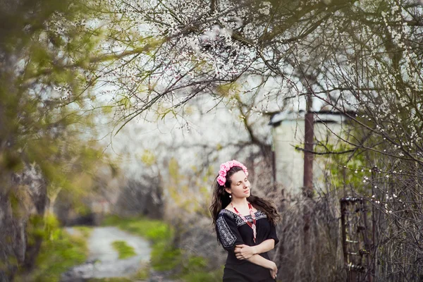Gyönyörű lány sétál a buja kertben öltözve egy koszorú — Stock Fotó