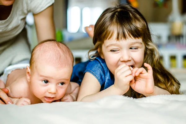 Menina bonito está brincando com seu irmão mais novo em casa deitado na cama — Fotografia de Stock