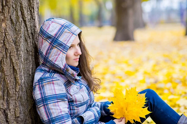 Młoda kobieta w jesień parku siedzi w pobliżu drzewa — Zdjęcie stockowe