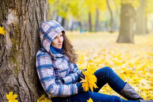Mujer joven en el parque de otoño sentado cerca del árbol — Foto de Stock