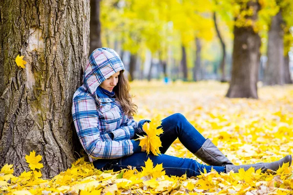 Młoda kobieta w jesień parku siedzi w pobliżu drzewa — Zdjęcie stockowe