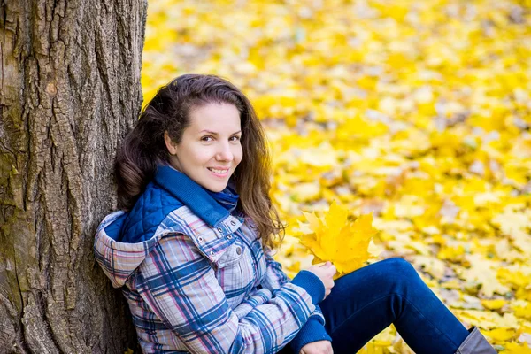 Νεαρή γυναίκα σε φθινόπωρο πάρκο κάθεται κοντά στο δέντρο — Φωτογραφία Αρχείου