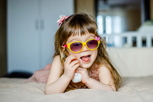 Niña de moda en gafas acostadas sobre su vientre y sonriendo — Foto de Stock