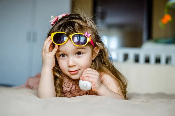 Moda bambina in occhiali sdraiata sul ventre e sorridente — Foto Stock