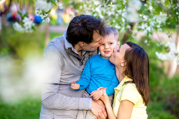 Feliz familia joven se encuentra cerca de un árbol floreciente y sonriente —  Fotos de Stock