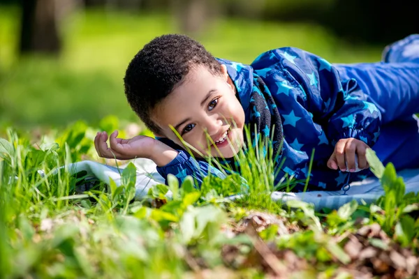 Cute happy little boy lying in green grass on spring — Stock Photo, Image
