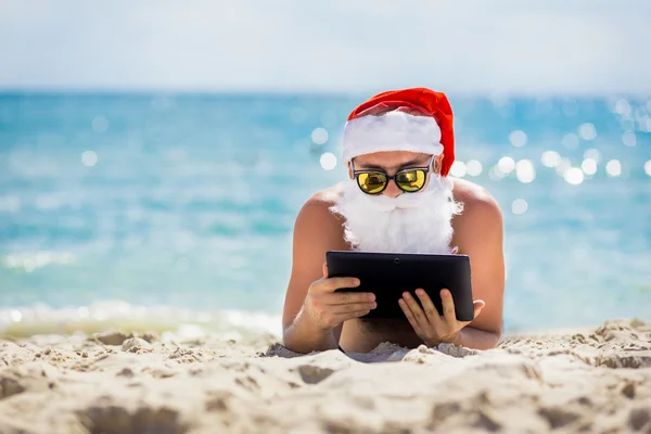 Święty Mikołaj na plaży z tabletem w ręce — Zdjęcie stockowe