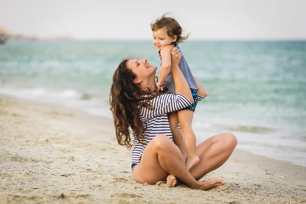 Joven hermosa madre y su adorable hijo se divierten en la playa . — Foto de Stock