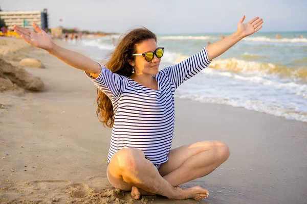 Mujer en la playa exótica en un suéter a rayas sentado con los brazos extendidos contra el mar turquesa. Turista despreocupado está disfrutando de vacaciones en la playa . — Foto de Stock