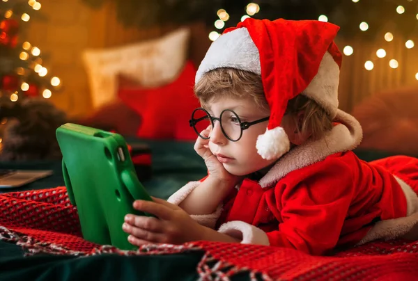 Garçon mignon en costume de Père Noël regarder des dessins animés de Noël sur tablette, se préparer pour la célébration, atmosphère merveilleuse et décorations, miracle — Photo