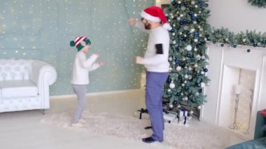 Baba küçük oğluyla Noel 'in tadını çıkartırken evdeki süslü bir odada parlak ışıklar ve bir Noel ağacıyla dans ediyor..