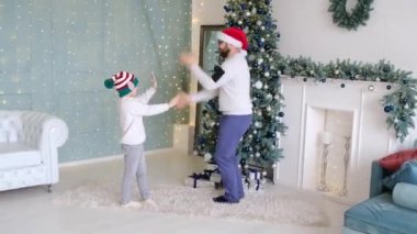 Baba küçük oğluyla Noel 'in tadını çıkartırken evdeki süslü bir odada parlak ışıklar ve bir Noel ağacıyla dans ediyor..