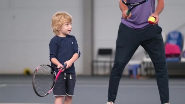 Erkek bir koç küçük bir çocuğa kapalı sahada oynamayı öğretir. Profesyonel bir tenis hocası bir çocuğa raket topu atar. KREMENCHUK, UKRAINE - 2 Ekim 2020: — Stok video