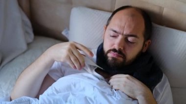 Adam yatakta, sıcaklığı kontrol ediyor. Yüksek ateşi olan biri termometreyi izliyor. Adam evde hasta..