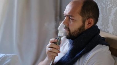 Koronavirüslü bir adam, grip, yatakta nebulizatör terapi solunum maskesi kullanıyor. Solunum tıbbı. Solunum astımı tedavisi. Bronşit, astım donanımı. Alternatif ev tedavileri.
