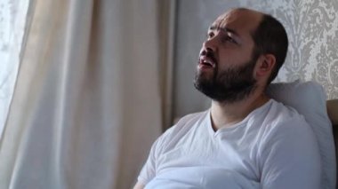 Aşırı büyümüş sakallı depresif bir adam evde ya da otel odasında yalnızdır. Üzgün, yorgun ve bitkin biri, zihinsel travma, hayal kırıklığı, kötü ruh hali, yalnızlık. Yan görünüm