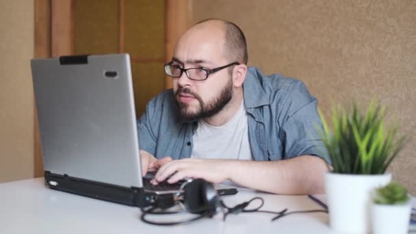 Сконцентрированный взрослый ботаник с бородой в очках, печатающий на ноутбуке, работающий над проектом, создающий программу или пытающийся взломать систему, показывающий жест "да", празднующий победу, фрилансер, телеработающий — стоковое видео
