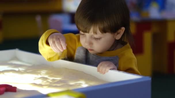 Lindo dibujo de niño dibuja arena en desarrollo en preescolar en la mesa en el jardín de infantes utilizando el método Montessori — Vídeo de stock