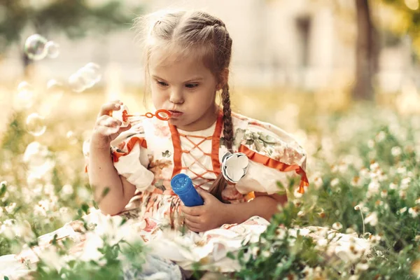 Een meisje met Down syndroom blaast bellen op. Het dagelijks leven van een kind met een handicap. Chromosomale genetische stoornis bij een kind. — Stockfoto