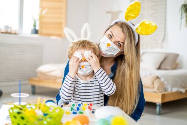 Koronavirüs salgını sırasında maskeli bir aile Paskalya yumurtası avında eğleniyor. Anne ve oğul, koronavirüs salgınını kutlamak için tavşan kulağı ve tavşan kostümü giyiyor. İyi tatiller..