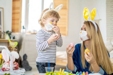 Koronavirüs salgını sırasında maskeli bir aile Paskalya yumurtası avında eğleniyor. Anne ve oğul, koronavirüs salgınını kutlamak için tavşan kulağı ve tavşan kostümü giyiyor. İyi tatiller..