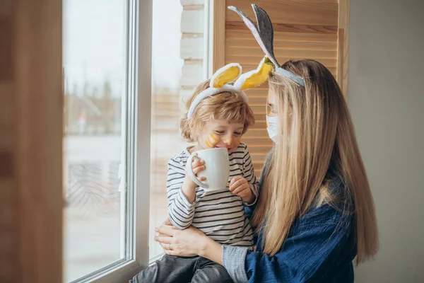 コロナウイルス発生中に楽しいマスク家族。ウサギの耳とウサギの衣装を着た母親と息子は、コロナウイルスのパンデミックを祝います。ハッピーホリデー. — ストック写真