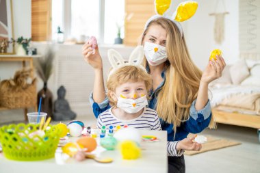 Mutlu anne ve oğul süslü tavşan maskesi takıyor kulaklık takıyor, Paskalya tatiline hazırlanıyor, aile karantina sırasında evde vakit geçiriyor.