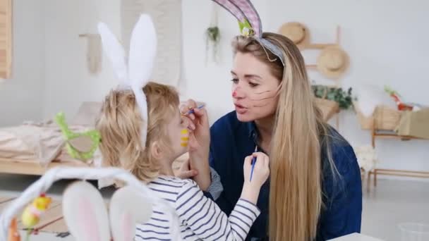 Beau fils heureux et la mère dans les bandeaux avec des oreilles de lapin décorer les œufs avec un pinceau et des peintures lumineuses, se préparer à célébrer Pâques, s'amuser à la maison — Video