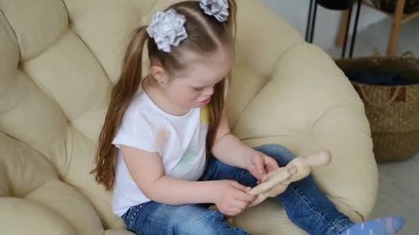 Pozytywne słodkie dziewczyny z zespołem Downa cieszy relaks na kanapie, zabawy i przytulanie drewnianej lalki, wyraża szczęście, radość i beztroski nastrój podczas relaksu w swoim pokoju. Codzienne życie — Wideo stockowe
