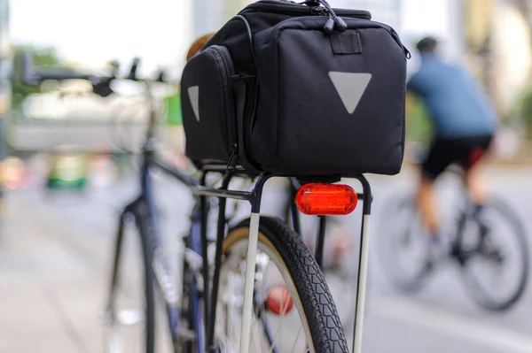 Close-up of illuminated bicycle tail light installed on bicycle rear rack and cyclist passing by on background