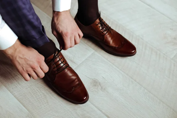A man ties his shoelaces. Brown shoes.
