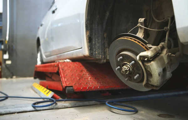 closeup car on a lift in a car service with a wheel removed. the technician is checking disk brake and brake caliper with soft-focus and over light in the background