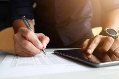 Ofiste çalışan bir iş adamı. Tablet üzerindeki bir e-postayı okuyarak ve kağıda yumuşak odaklı notlar alarak arka plandaki ışığın üzerine konuyor.