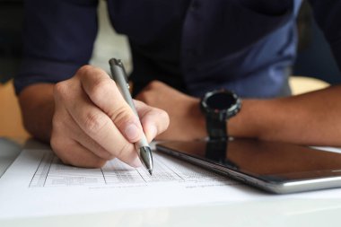 Ofiste çalışan bir iş adamı. Tablet üzerindeki bir e-postayı okuyarak ve kağıda yumuşak odaklı notlar alarak arka plandaki ışığın üzerine konuyor.