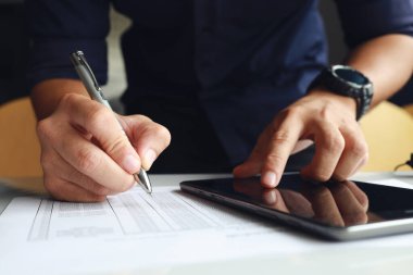 Ofiste çalışan bir iş adamı. Tablet üzerindeki bir e-postayı okuyarak ve kağıda yumuşak odaklı notlar alarak arka plandaki ışığın üzerine konuyor.
