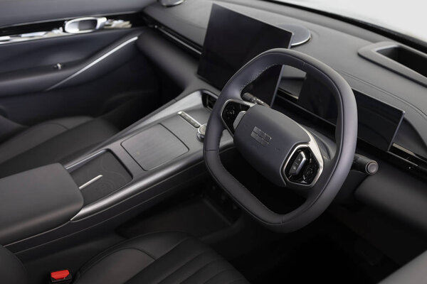 Крупный план футуристической, темной внутренней кабины Geely EX5, подсветка кожаного рулевого колеса, сенсорного дисплея и гладкой приборной панели модели электромобиля.