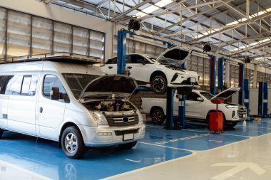 Elektrikli ve hibrit araçlar profesyonel oto tamir atölyesinde bakım görüyor. Hidrolik asansörler, teşhis araçları ve temiz, iyi aydınlatılmış garaj ortamı..