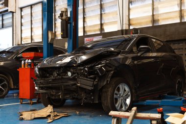 Çarpışma onarımı ve sigorta tazminatı için garajda tamponu eksik, buruşmuş siyah bir araba..
