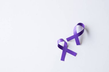 Beyaz bir yüzeyde iki mor kurdele Alzheimer, aile içi şiddet ya da geniş kopya alanı olan pankreas kanseri farkındalığını simgeliyor..