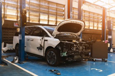 Sigorta tamiri için profesyonel bir garajda asansörde açık kaput ve yan çarpma hasarı olan beyaz elektrikli araç..