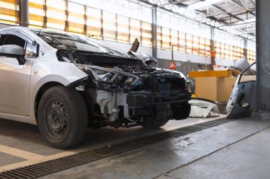 Otomobil tamirhanesindeki hasarlı araba çarpışmadan sonra tamponu sökülmüş araç bakım sigortası tazminatı ve kaza onarımı konseptini temsil ediyor..