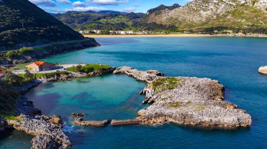İspanya 'nın Cantabria kentindeki Playa de Berria yakınlarında dağlarla çevrili bir turkuaz lagün ve kayalık yarımadanın havadan görünüşü.