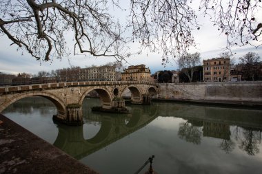 Zarif Ponte SantAngelo, İtalya 'nın Roma kentindeki tarihi SantAngelo Kalesi' ne doğru uzanan sakin Tiber Nehri boyunca uzanır. Dramatik gökyüzü ve sudaki yansımalar sonsuz şehrin kalbinde sakin ama görkemli bir atmosfer yaratıyor..