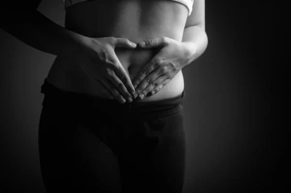 Manos de mujer joven conformando un corazón en el ombligo primer plano, blanco y negro — Foto de Stock