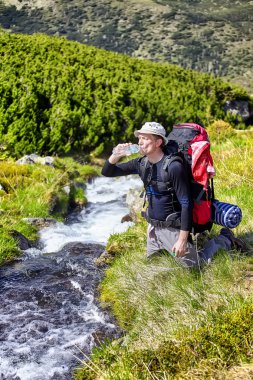 Dağ nehir kenarında rahatlatıcı ve şişelenmiş su içme uzun yürüyüşe çıkan kimse